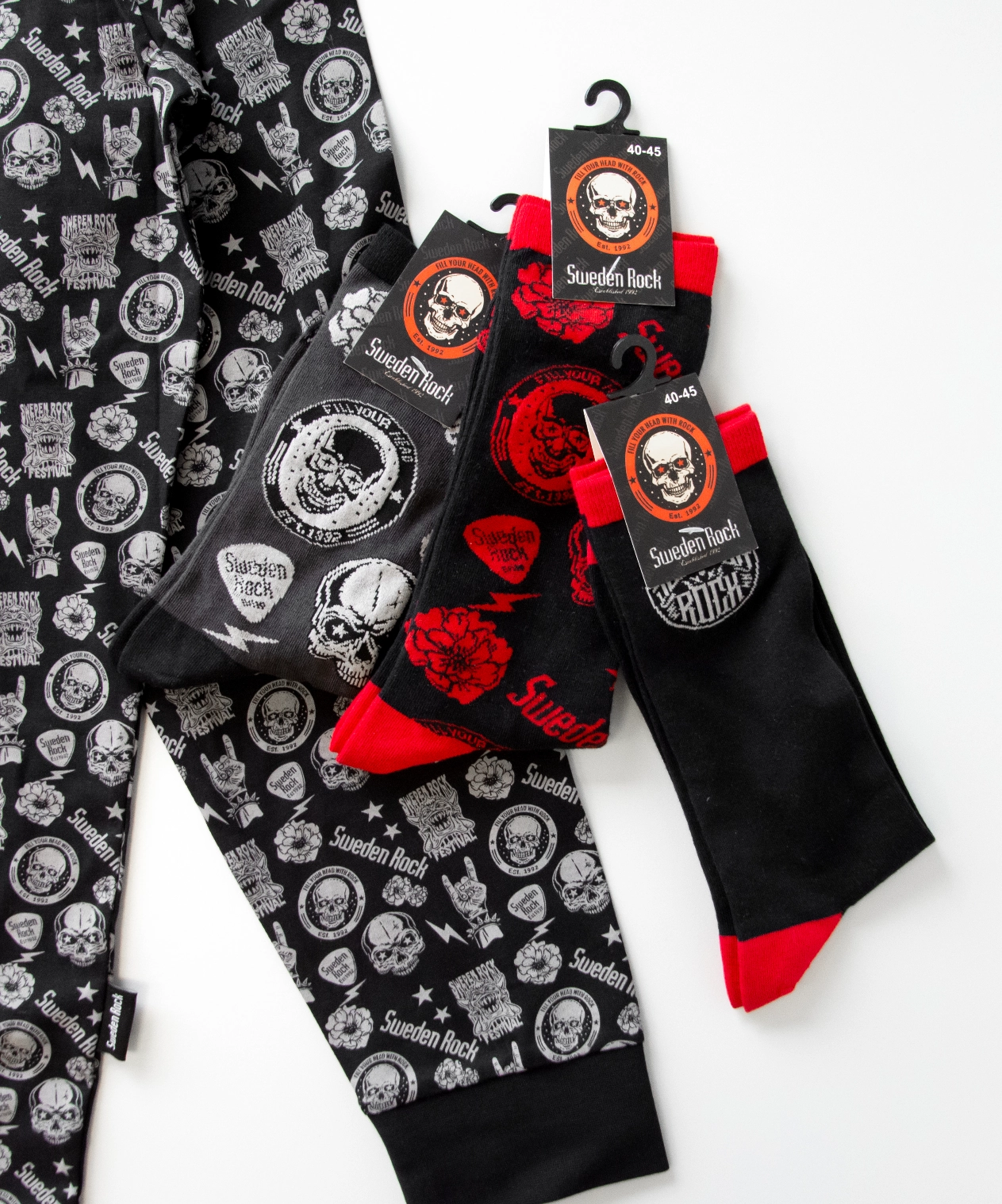 Ett par svarta och vita mönstrade mjukisbyxor eller pyjamasbyxor från Sweden Rock Festival visas bredvid tre par svarta och röda Sweden Rock-strumpor med grafik som föreställer dödskallar och logotyper